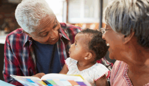 Smiling grandparent caregivers hold their granddaughter while they read her a book.