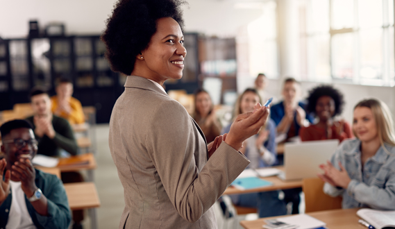A woman leads a presentation in class as adults students applaud.