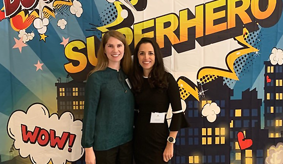 Executive Director Patricia Lozano and Senior Policy Advisor Stephanie Tseu pose in front of a Superhero banner.
