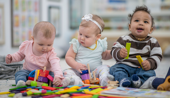 Babies play near each other on a daycare carpet.