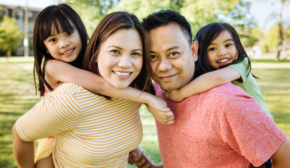 Smiling Filipino parents hold each of their daughters on their backs.