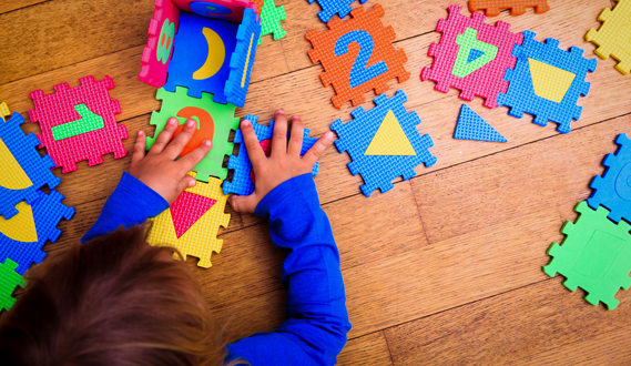 A child plays on the floor with number and letter foam tiles.