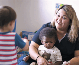 A provider holds a toddler in her lap while speaking with another young student.