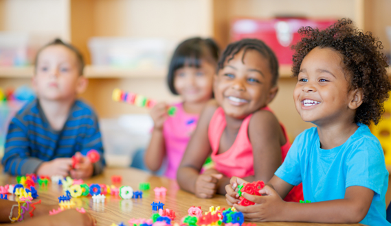 Young elementary students smile as they play with Legos at a table in class.