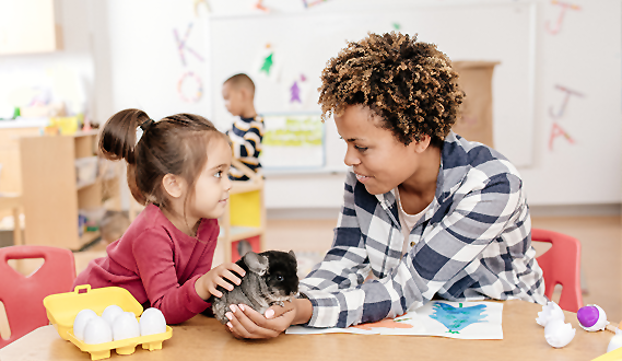 A woman holds a kitten as a preschool student gently pets it