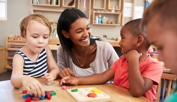 A teacher smiles at a yound student as they practice with block wooden letters