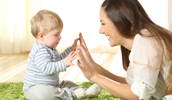 A daycare provider holds her hands up to a baby's while smiling.