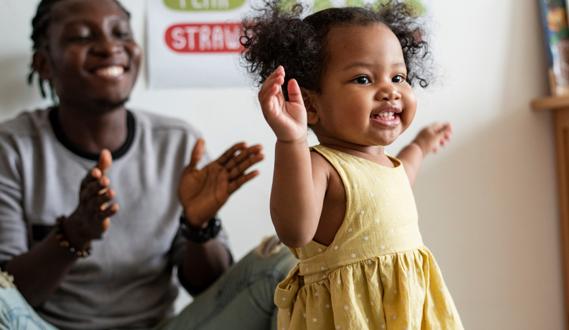 A daycare provider claps as a baby stands by herself.