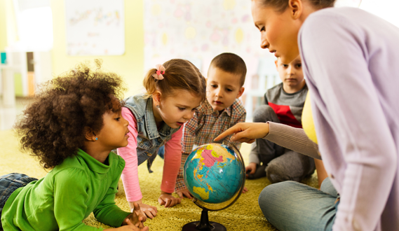 A teacher points at a globe while her young students look at it.