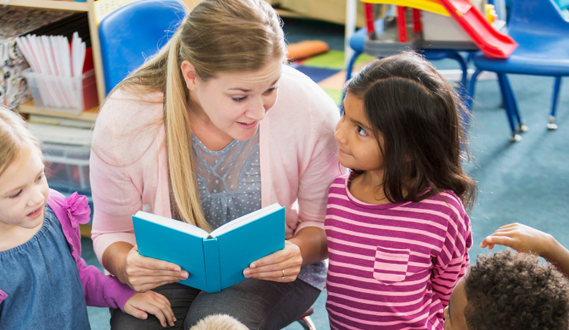 A teacher reads to a student while she looks at her with deep focus.