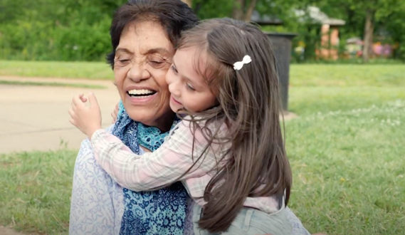 A young girl hugs an older woman who smiles.