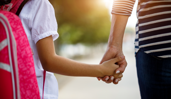 A mother holds her child's hand as they walk to school.