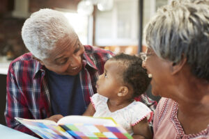Smiling grandparents read a book with their infant granddaughter.