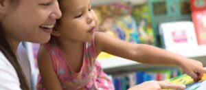 A  young child points to something on a desk as her teacher looks on.