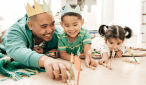 An AAPI father in a crown plays with his young son and daughter.