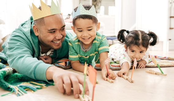 An AAPI father in a crown plays with his young son and daughter.