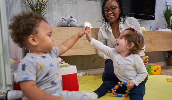 2 toddles high five as a home daycare provider looks on smiling.