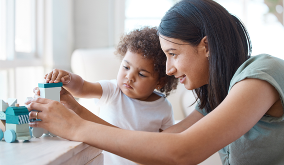An in-home child care provider helps a toddler with blocks.
