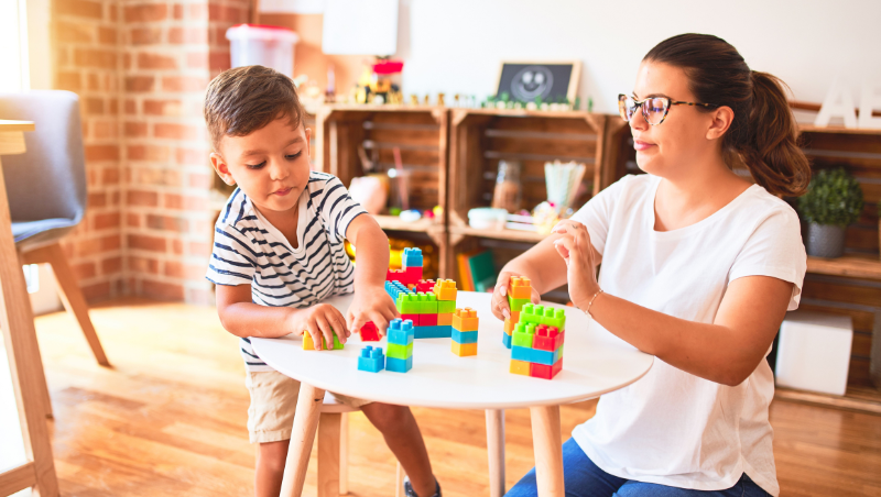 A caregiver and a preschool age buy play with Legos.