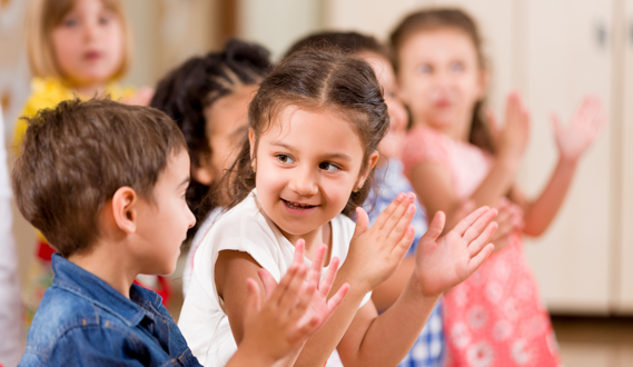 Young children stand in a row clapping their hands.