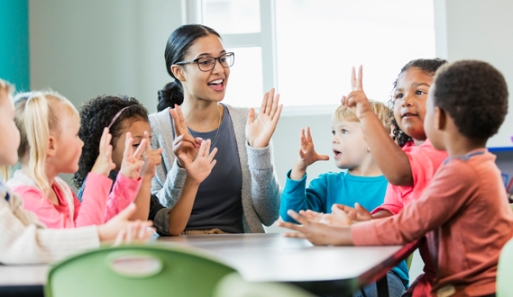 A teacher sings a counting song with young students at a round table.