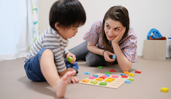 An in-home daycare provider plays on the floor with a young boy.