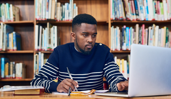 A college student takes notes as he works in a library.