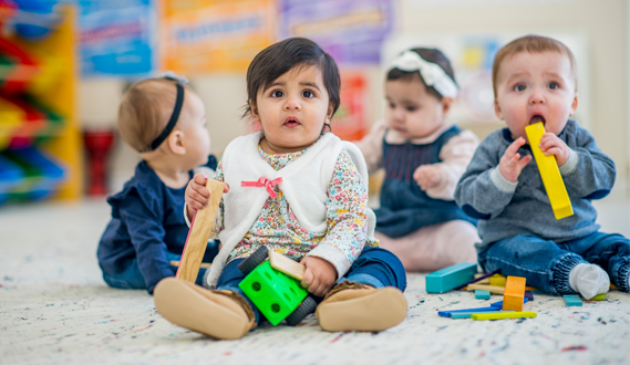 Babies sit on a carpet playing at a childcare facility.