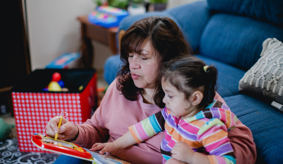 An in-home childcare provider plays a game with a preschooler on her coffee table.