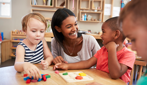 A teacher smiles at a student as they use block letters.