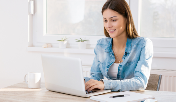 A woman takes notes while using her laptop.